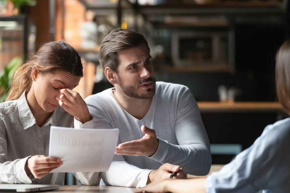 Stressed couple reviewing paperwork while speaking with an advisor about unexpected ownership costs.
